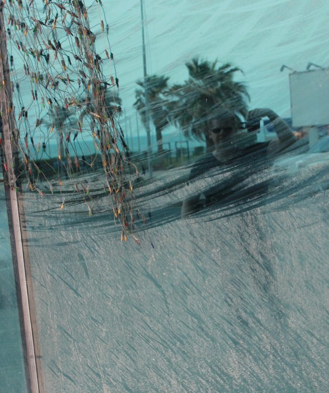 A selfie taken in a window, my reflection in the dust scraped off its surface by wind blowing strands of Christmas lights .