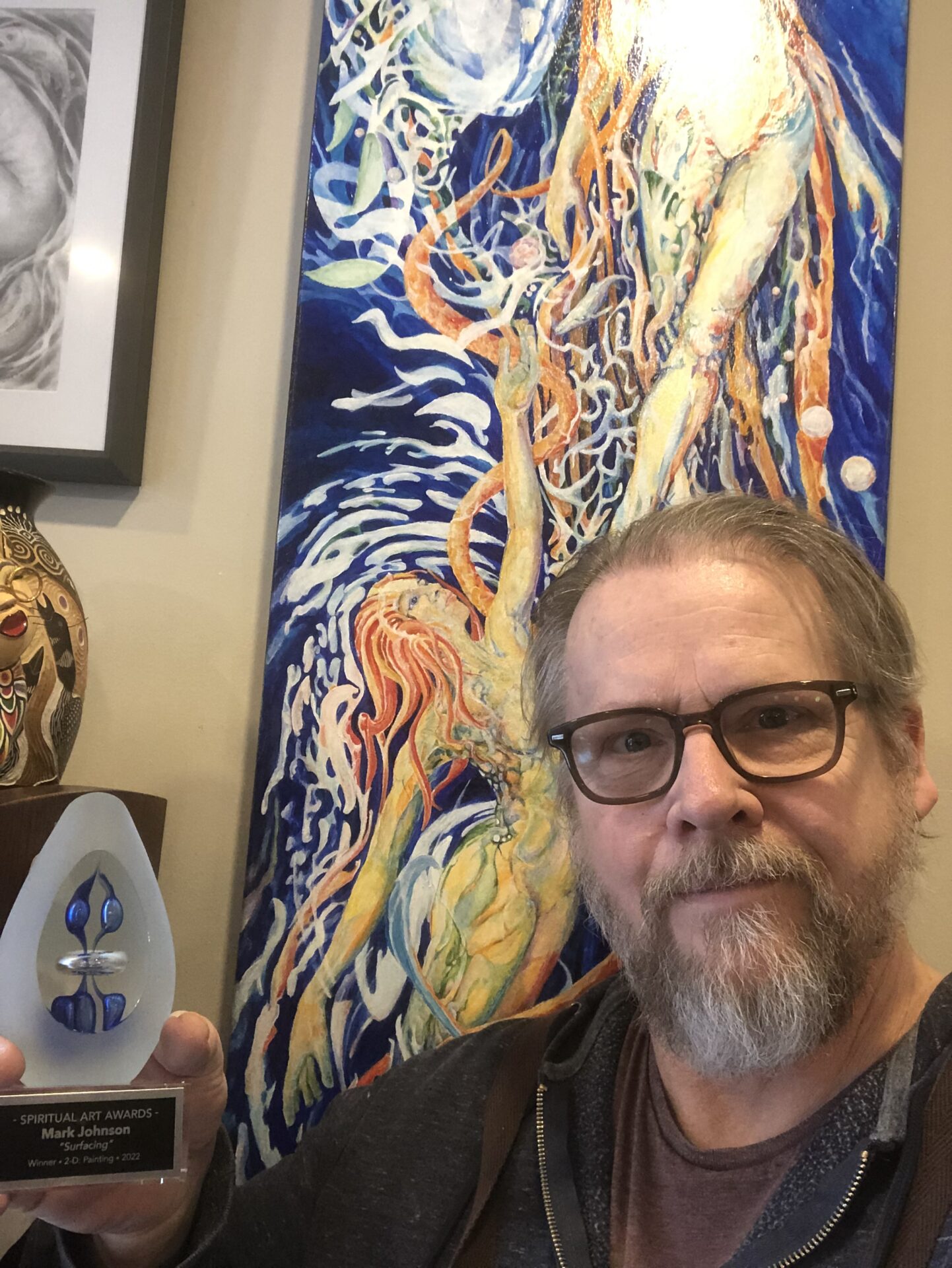 Bearded man holding award before colorful painting